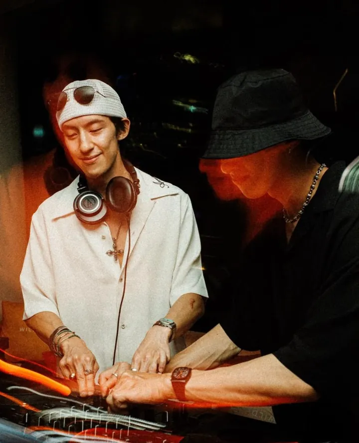 Twin Dragons mid-set: the two brothers bent over one mixer, four hands on the decks at once, lit in red and amber.